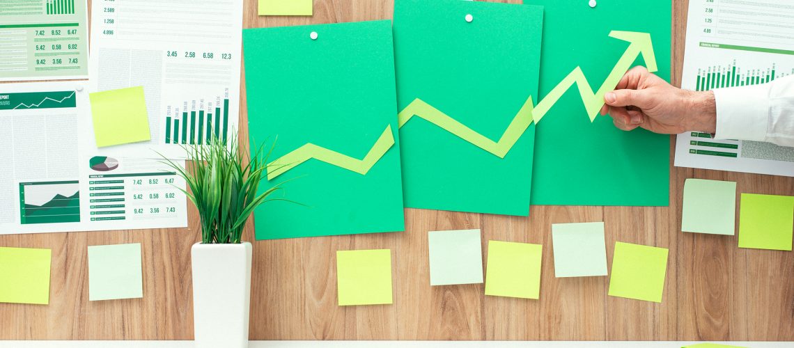 Businessman composing a successful financial chart with arrow going up, he is using green paper cuts, eco business and financial success concept